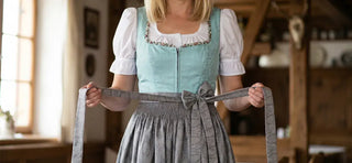 Woman tying a dirndl apron bow on a traditional Bavarian dirndl dress.