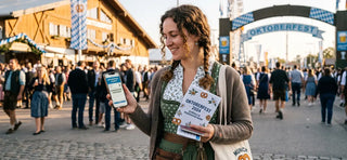 Oktoberfest 2026 visitor holding digital tickets and an official schedule and reservation guide.