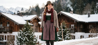Woman wearing a winter Dirndl outfit with a cardigan, scarf, and hat in a snowy Bavarian village.