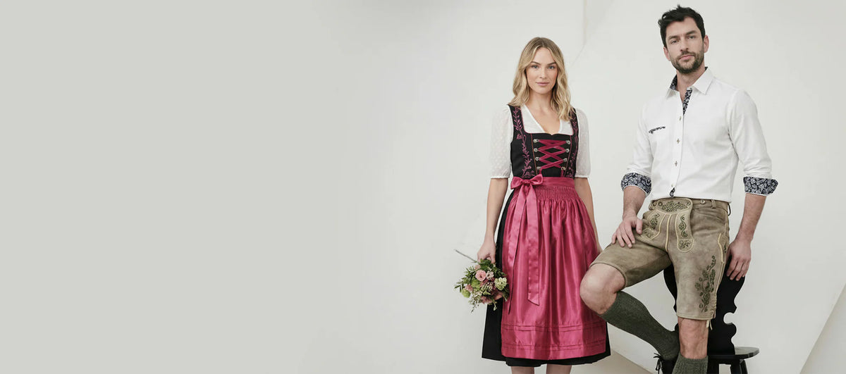 Woman in black dirndl with pink apron and man in lederhosen, traditional Oktoberfest outfits.